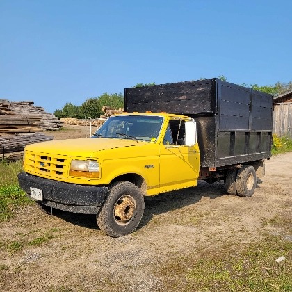 a yellow dump-truck with a black box parked on a dirt road